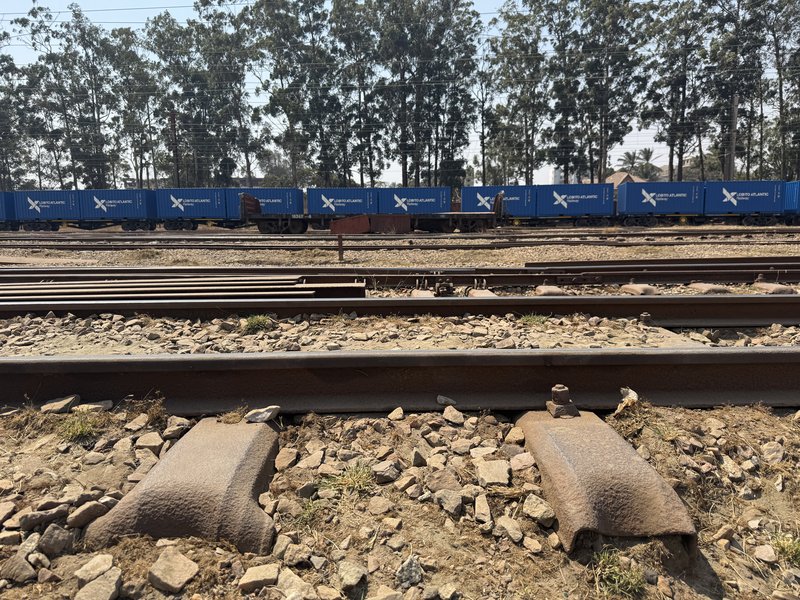 Railway sleepers can be seen in the foreground, with a line of blue railway wagons marked Lobito Atlantic Railway on the tracks behind