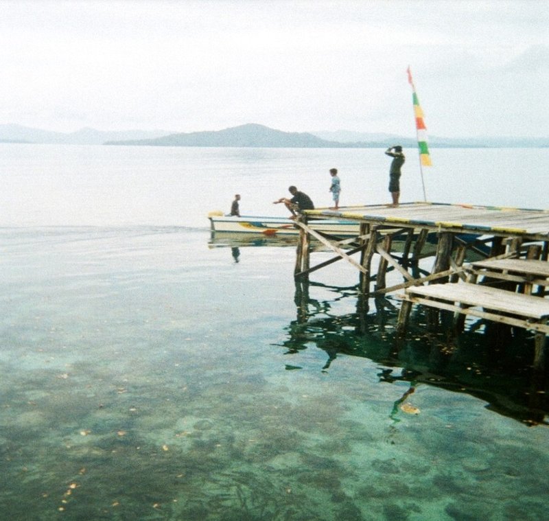 View of pier on Mutus with the coral visible in the foreground underwater and a child on the pier