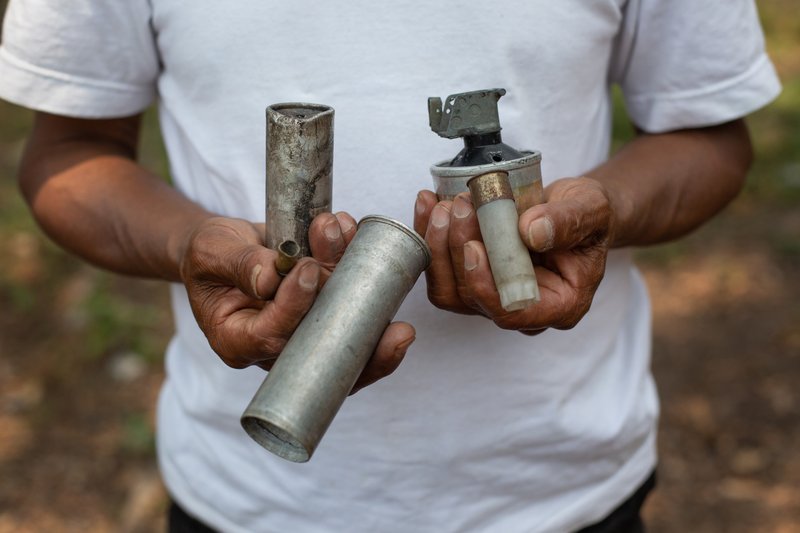 An Indigenous activist holds smoke bombs, tear gas canisters and other projectiles used by Guatemalan state authorities to prevent peaceful protest against a hydro-electric project